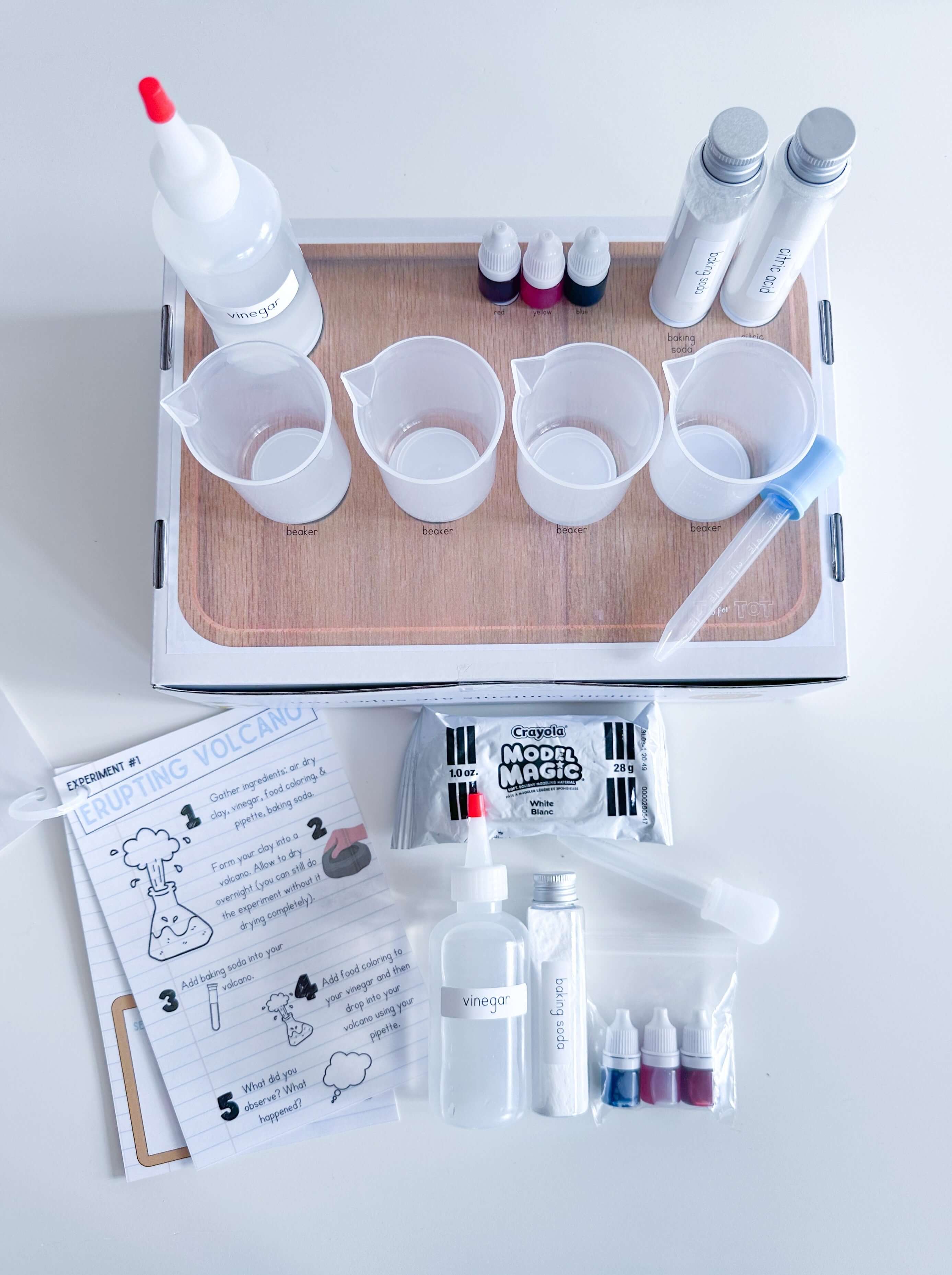 Science-themed play and learn kit for kids with a lab coat, beakers, pipettes, and food coloring. Includes an experiment guide, dry erase marker, art supplies, and homemade playdough with a lab playdough cutter. Ideal for science experiments and creative play.