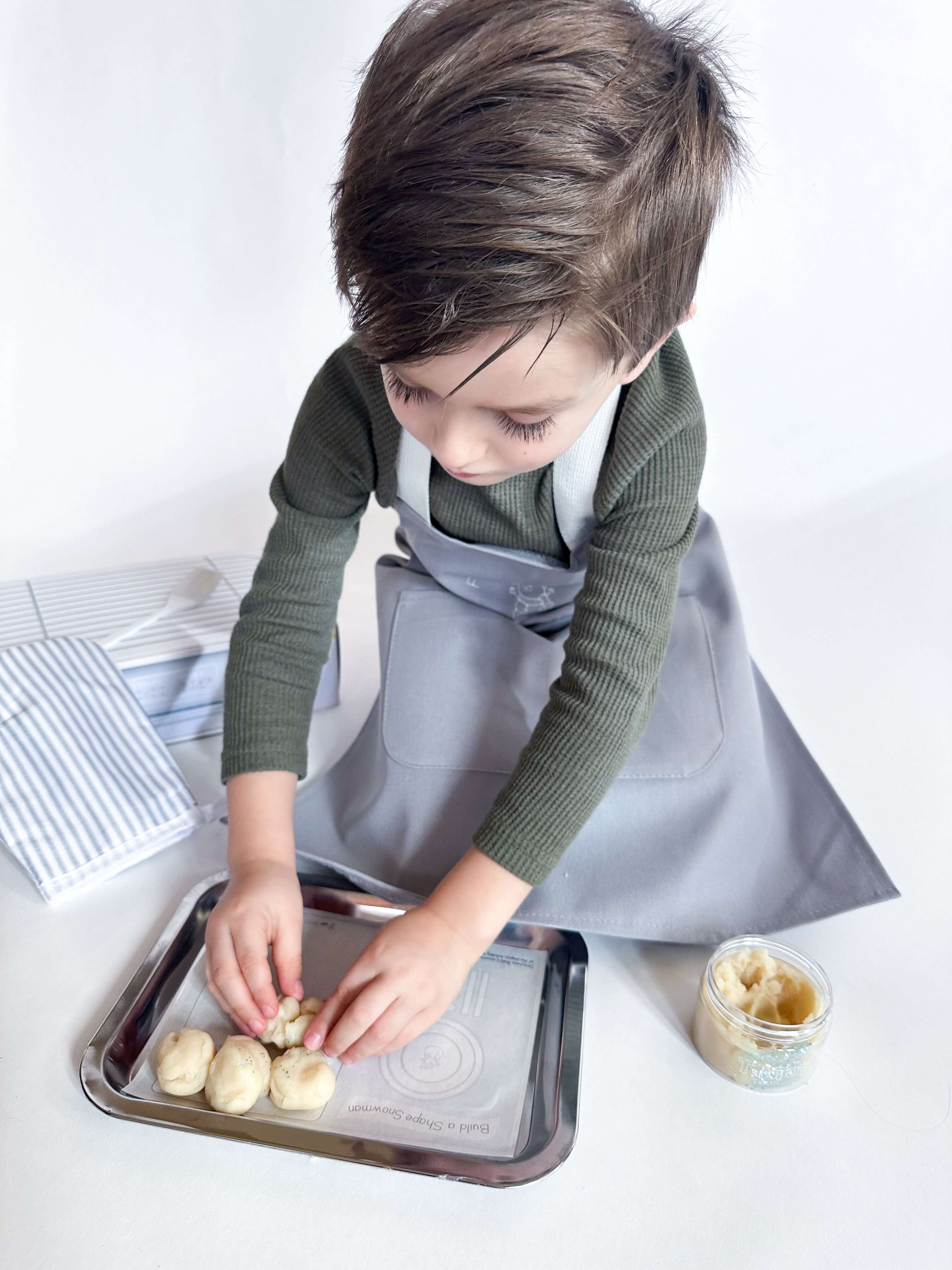 Preschool-aged child wearing an apron, using baking tools from the Frosty Fun Baking Kit